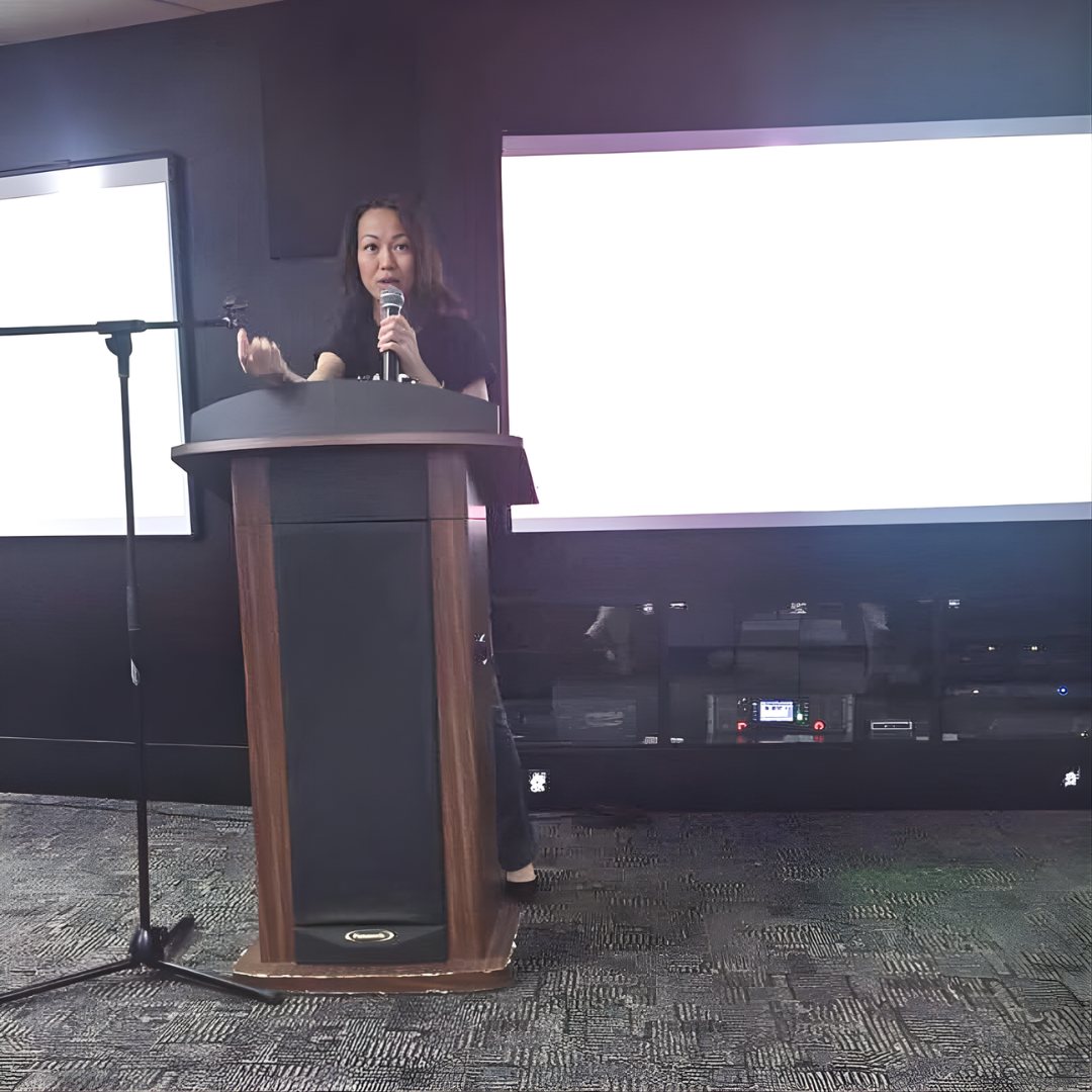 Therine Goh delivering a corporate talk at a podium using a microphone